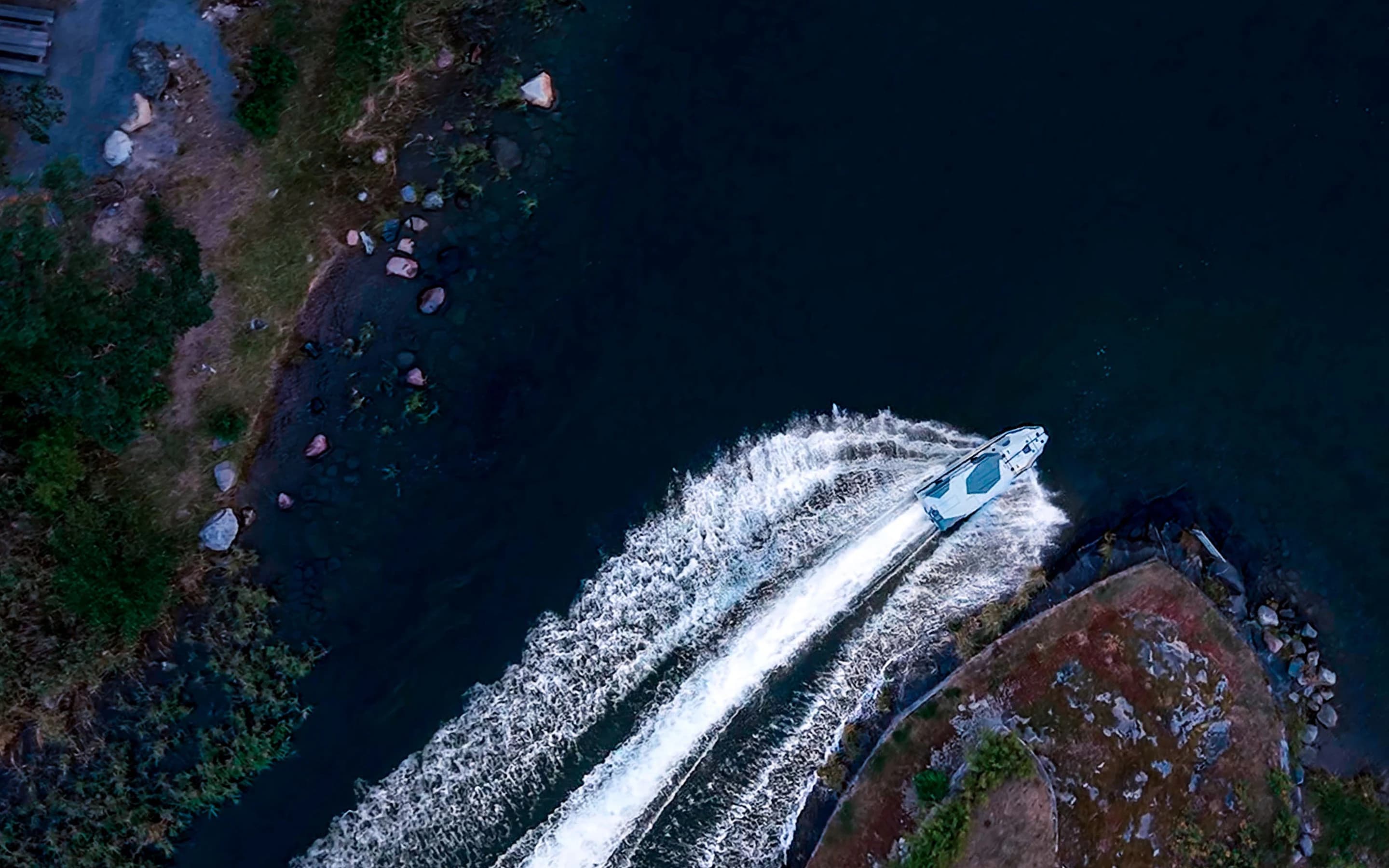 Aerial view of a Nautrik vessel carving a white wake past a rocky shoreline