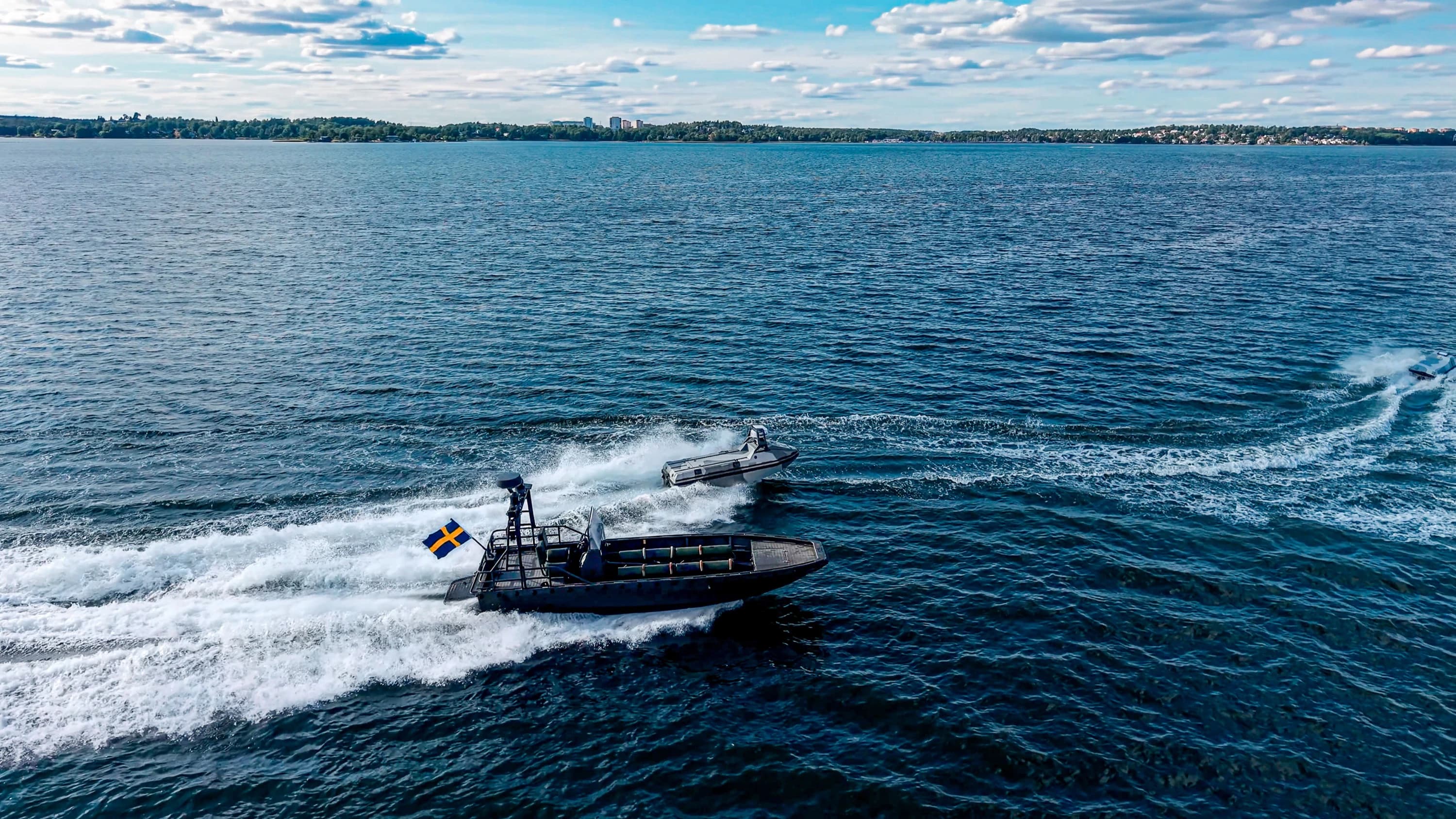 A Nautrik uncrewed surface vessel running alongside a crewed boat flying the Swedish flag